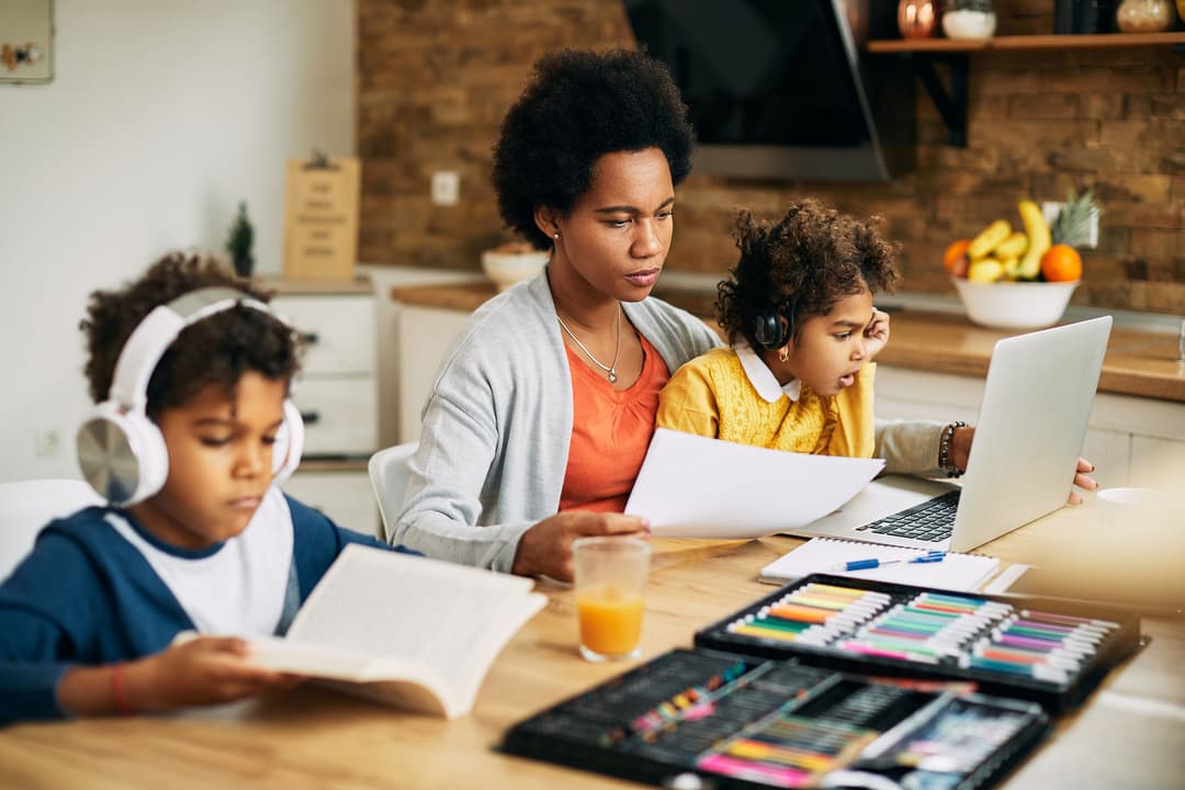 A mother homeschooling two children at the kitchen table